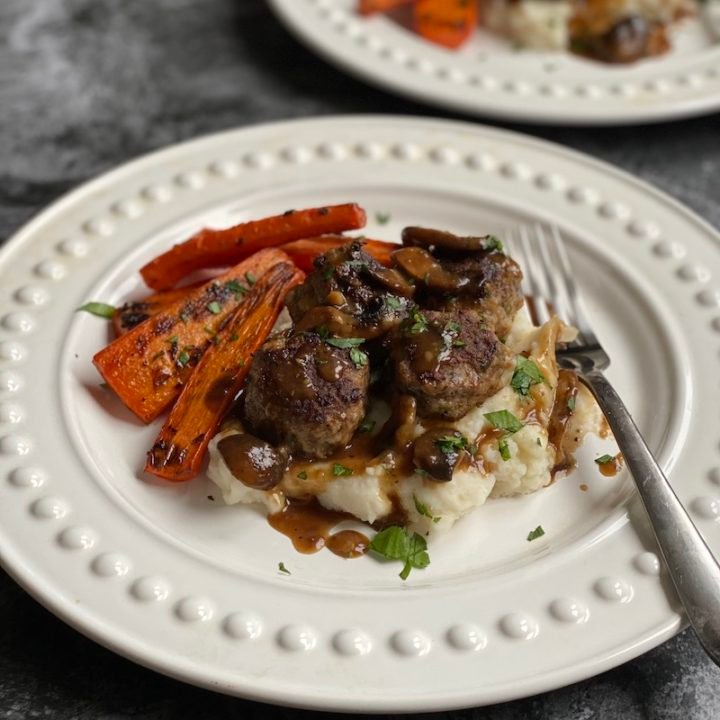 this is a photo of salisbury steak with mushroom gravy over mashed potatoes and roasted carrots