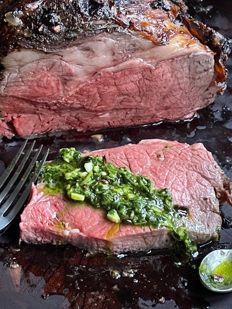 This is a photo of sliced oven roasted standing rib roast with chimichurri sauce