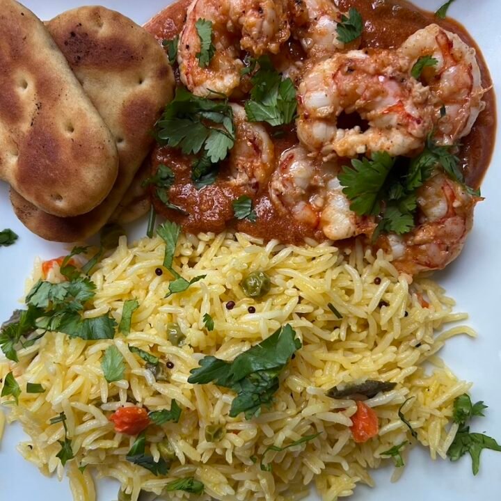 This is a plate of shrimp tikka masala with rice and naan.